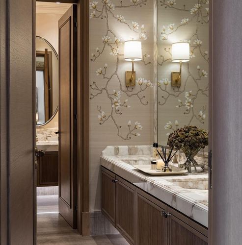 Powder bathroom with floral wallpaper, marble vanity, brass sconces, seen through open wooden door