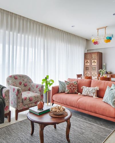 Living room with coral sofa, floral armchair, carved wood cabinet and sheer curtained wall