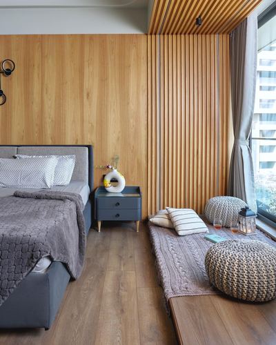 Bedroom with slatted wood wall, grey upholstered bed, and knitted poufs by a window seat