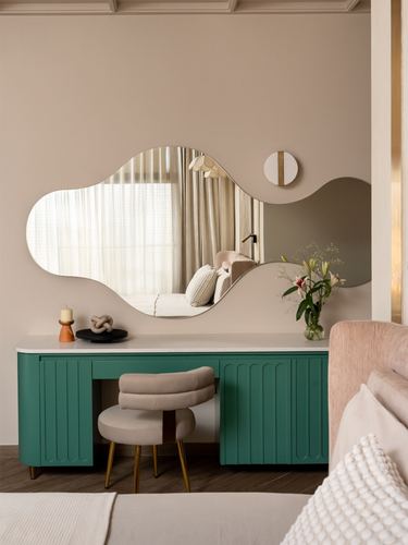 Blush bedroom with wavy mirror over fluted teal green vanity and cushioned stool