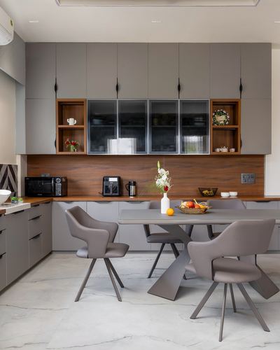 Grey kitchen with wood backsplash, fluted glass cabinets, and a dining table with cane-back chairs