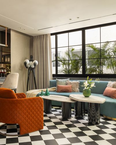 Living room with teal sofa, orange quilted armchair, marble coffee tables and checkerboard floor