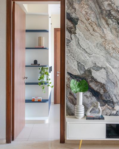Open wooden door revealing shelving nook beside a veined stone-clad wall with console and vase