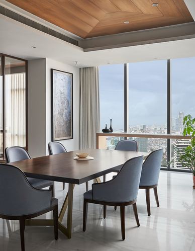 Dining room with wood ceiling, blue chairs around dark table, city skyline through glass wall