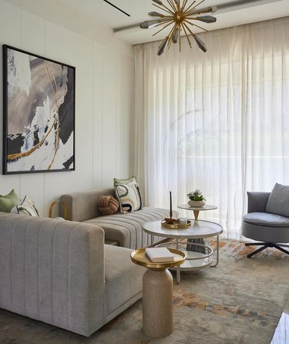 Neutral living room with sectional sofa, marble coffee tables, sheer curtains and brass chandelier