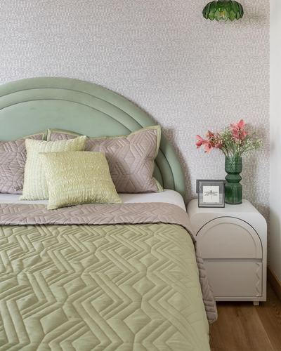 Sage green arched headboard bed with pink and green pillows beside a rounded nightstand with flowers