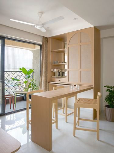 Light wood breakfast counter with cane-backed stools beside an arched storage cabinet and balcony
