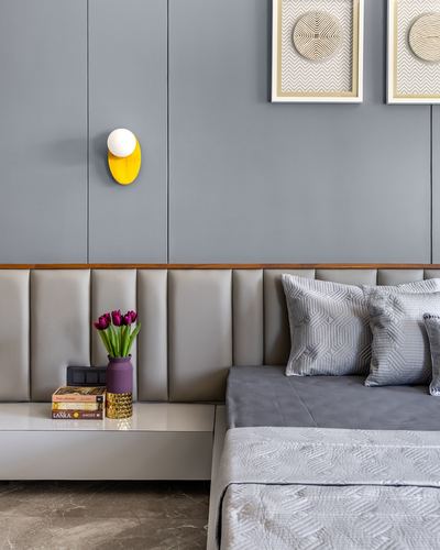 Grey channel-tufted headboard with bedside table holding books, vase of tulips, and wall sconce above
