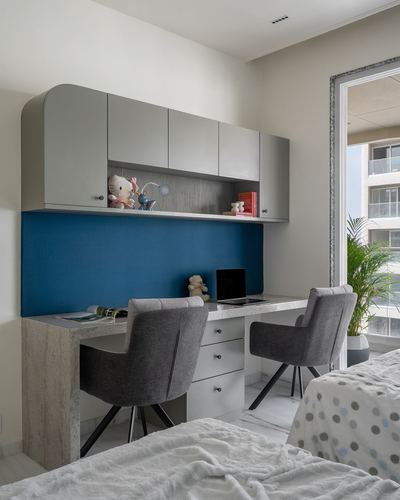 Kids' study nook with twin desk, gray cabinets, and a blue upholstered backsplash