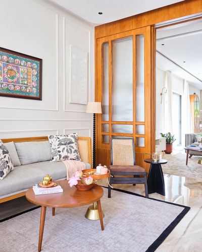 Living room with teak sliding door, cane chair, round wood coffee table, and framed thangka art