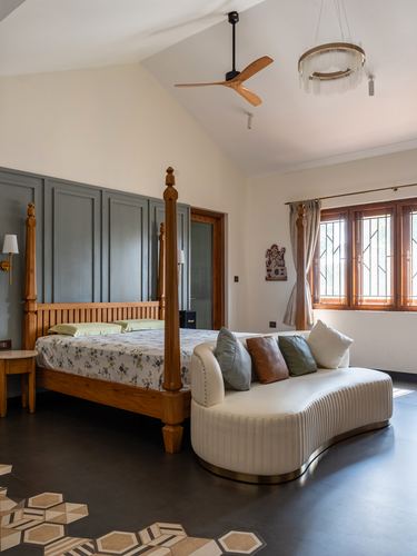 Bedroom with wooden four-poster bed, curved cream sofa, and vaulted ceiling with fan and chandelier