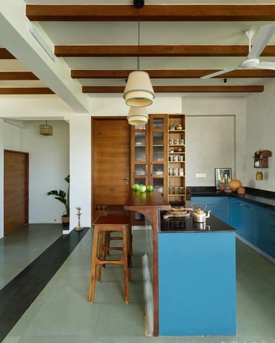 Kitchen with wooden beamed ceiling, teal cabinetry, wooden stools, and pendant lights over breakfast counter