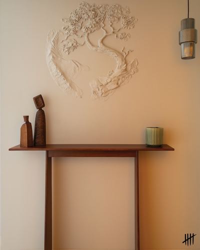 Wooden console table below a textured tree relief sculpture and pendant light