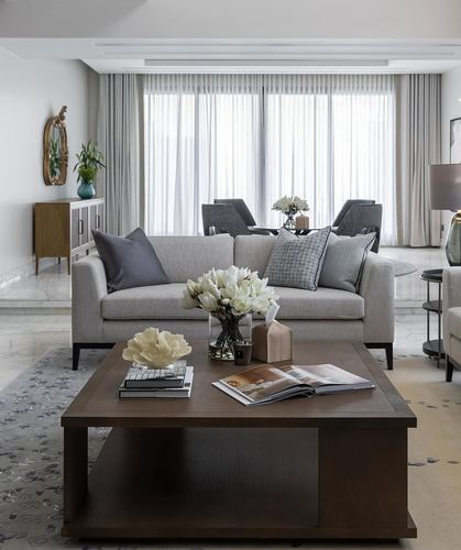 Neutral living room with grey sofa, dark wood coffee table, and sheer-curtained windows behind