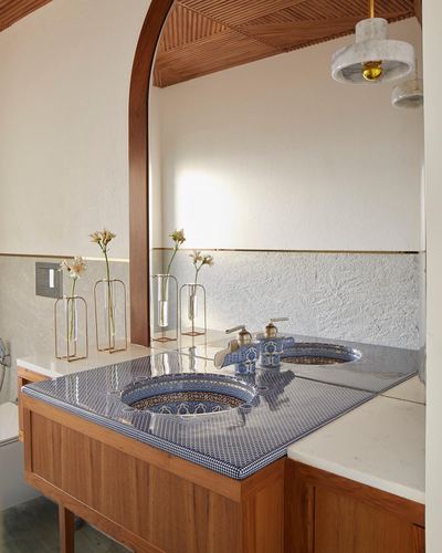 Bathroom vanity with two blue-patterned ceramic basins under an arched wooden mirror frame and marble pendant light