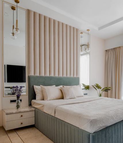 Bedroom with fluted beige upholstered wall, sage velvet bed, brass pendant lights and mirror