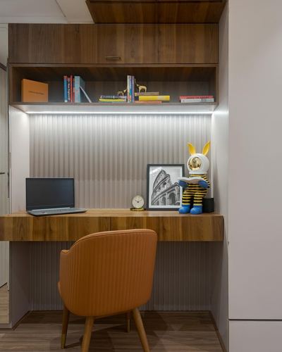 Built-in wooden desk nook with open bookshelf, laptop, decor, and orange upholstered chair