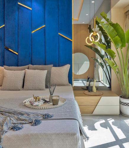 Bedroom with blue fluted headboard, brass accents, and a mirrored nook with large plant beyond