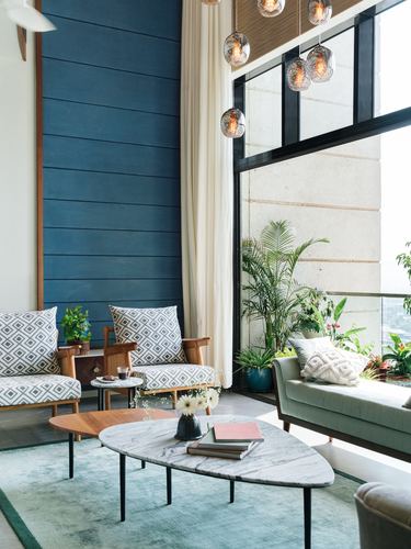 Double-height living room with blue paneled wall, marble tables, patterned armchairs and glass pendant lights facing balcony