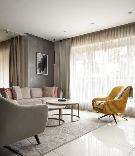 Neutral living room with grey sectional, mustard velvet chair, and nesting marble coffee tables by sheer-curtained window