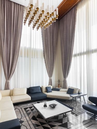 Double-height living room with layered curtains, brass pendant cluster, and cream-charcoal sectional on inlaid marble floor