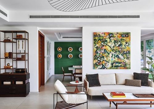 Living room with beige sofa, wire chair, and large colorful abstract painting on white wall
