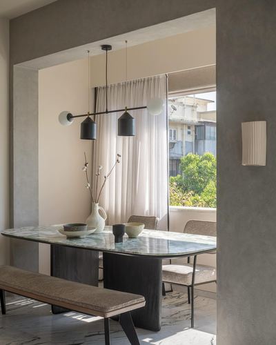 Dining nook with marble table, dark wood base, twin pendant lights, and sheer curtains framing a balcony view