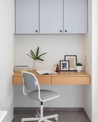 Floating wood desk with grey chair under pale blue cabinets in a small study nook