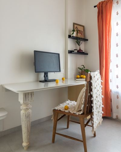 Wall-mounted study desk with monitor, turned legs, wooden chair with textured throw, orange curtain