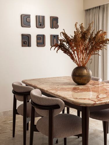 Dining table with peach marble top, boucle chairs, dried flowers, wall art sculptures