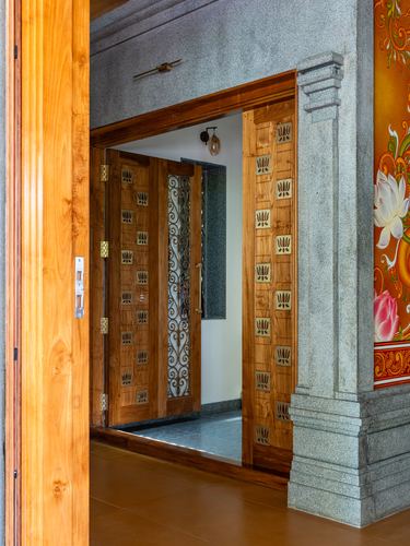 Carved wooden doors with lotus motifs open through a granite frame into a foyer