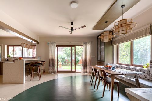 Open dining and kitchen area with rattan pendants, wooden table, and green terrazzo floor facing garden