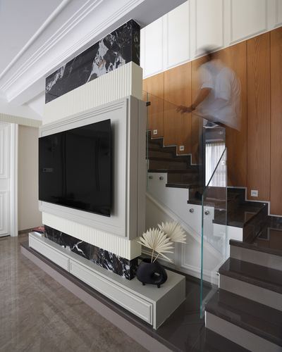 TV wall with black marble accents beside a wood-paneled staircase, person walking up blurred