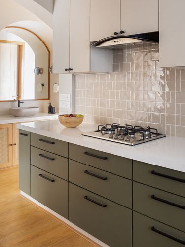 Kitchen island with olive drawers, white countertop, gas hob, and glazed tile backsplash beside an arched niche