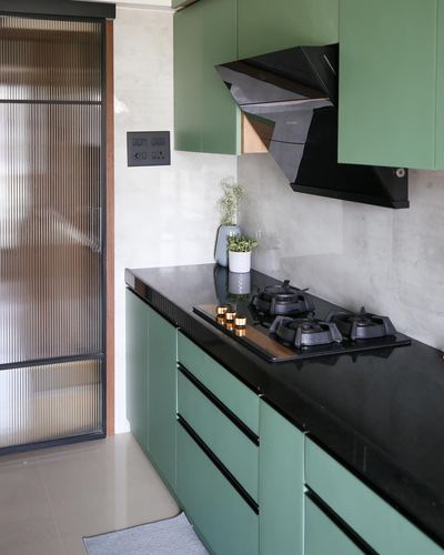 Sage green kitchen with black stone counter, chimney hood, and reeded glass sliding door