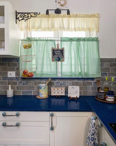Kitchen counter with blue speckled countertop, brick-look backsplash, and green sheer curtains at window