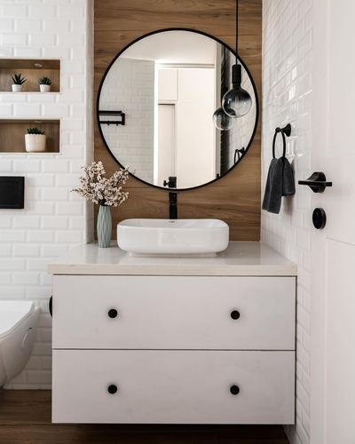 White bathroom vanity with round black-framed mirror against wood wall and subway tile