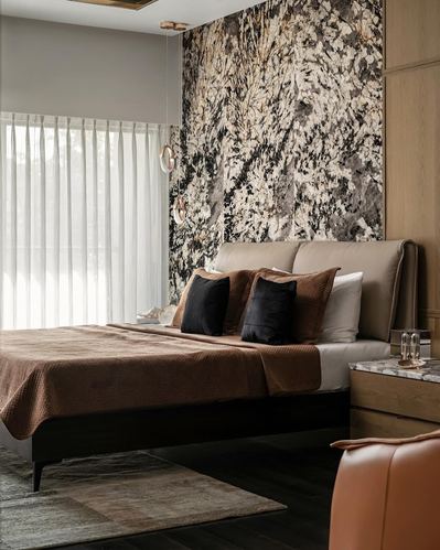 Bedroom with veined stone accent wall behind upholstered bed and rust leather chair