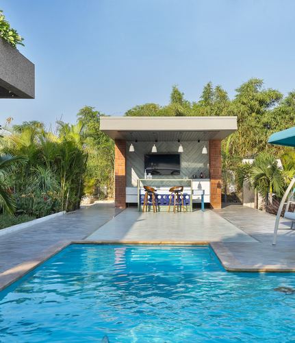 Poolside cabana with outdoor bar, TV, and pendant lights surrounded by tropical greenery