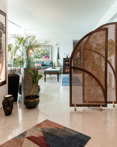 Foyer with arched cane screen, potted plants, sculptural bust and patchwork rug leading to living room