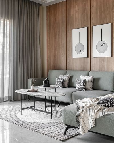 Sage sofa against wood-panelled wall with oval stone coffee tables on layered rug