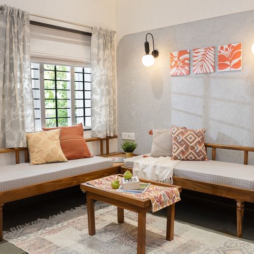 Corner living room with teak daybeds, textured grey wall, and orange botanical art