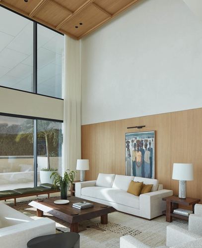Double-height living room with wood-panelled lower wall, white sofas, and a figurative painting above a wood console