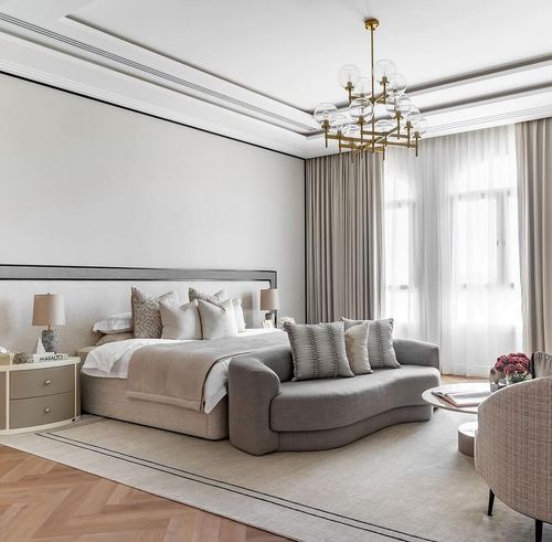 Neutral master bedroom with upholstered headboard, curved grey sofa, and brass bubble chandelier