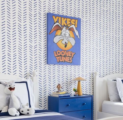 Kids bedroom with blue herringbone wallpaper, twin beds, and a Looney Tunes canvas above a blue nightstand