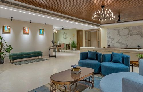Living lounge with blue armchairs, oval brass coffee table, and marble wall under wood-slat ceiling