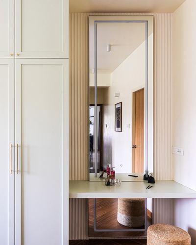 Dressing nook with tall mirror, fluted panelling, stone counter, and jute pouf beside wardrobes