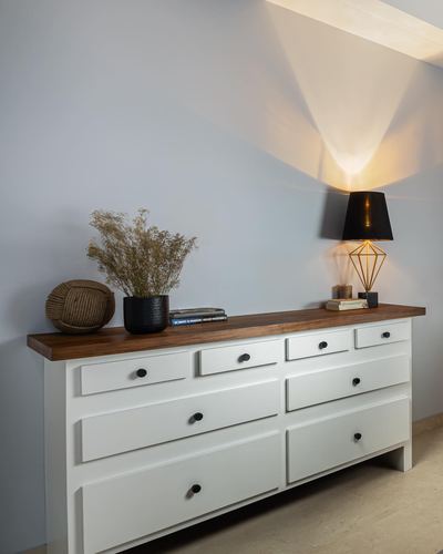 White console table with wood top, black lamp, dried flowers, against grey wall
