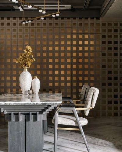 Dining table with marble top and carved wood base against a glowing perforated bronze grid wall