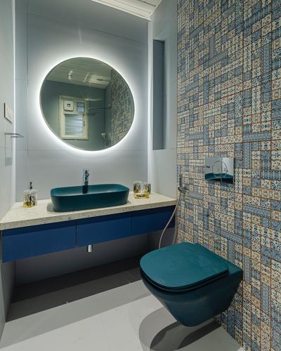Small bathroom with round backlit mirror, teal vessel sink, and patchwork tile wall behind teal wall-hung toilet.